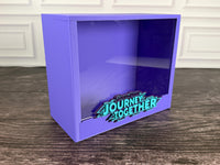 Purple Journey Together ETB display case, angled view with raised turquoise logo